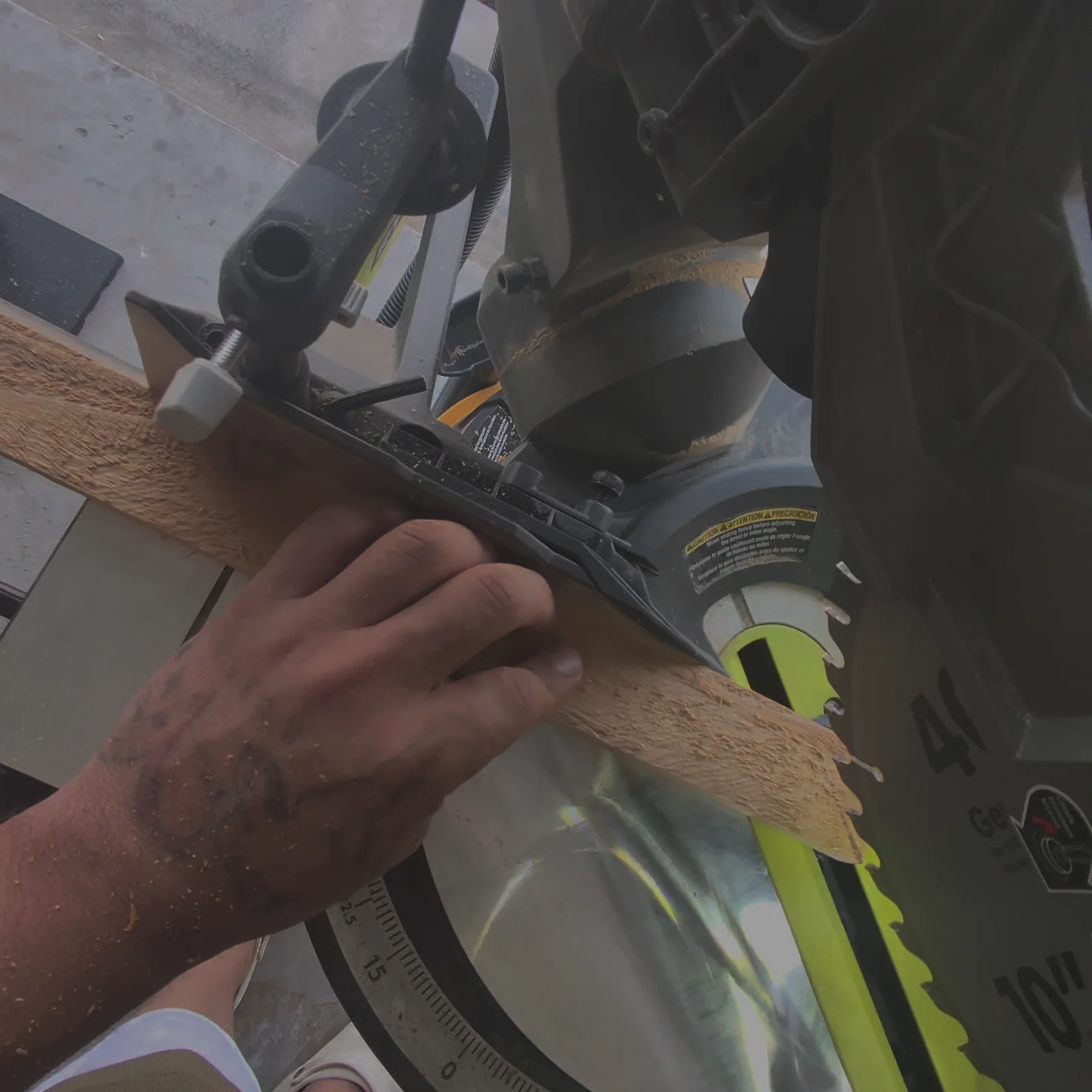 The miter saw blade lowered into a cedar board, a hand holding the board against the fence
